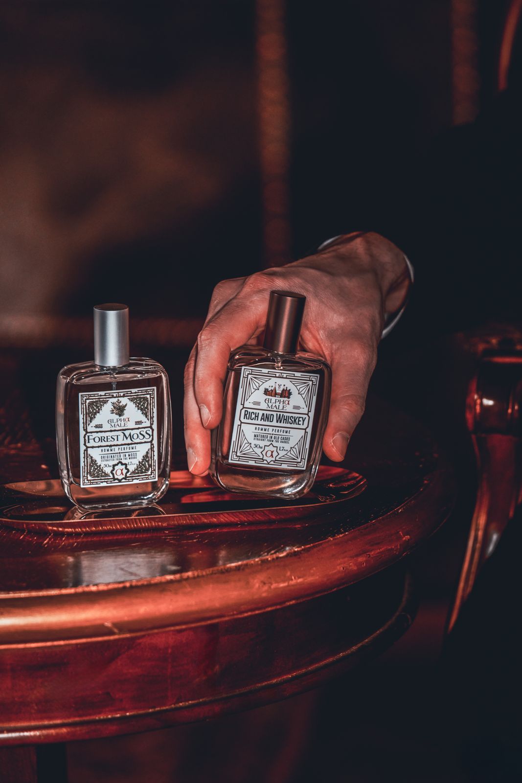 ALPHAMOOD · 모델촬영 — 원형 테이블 위 Forest Moss·Rich and Whiskey 두 제품에 손을 뻗는 컷