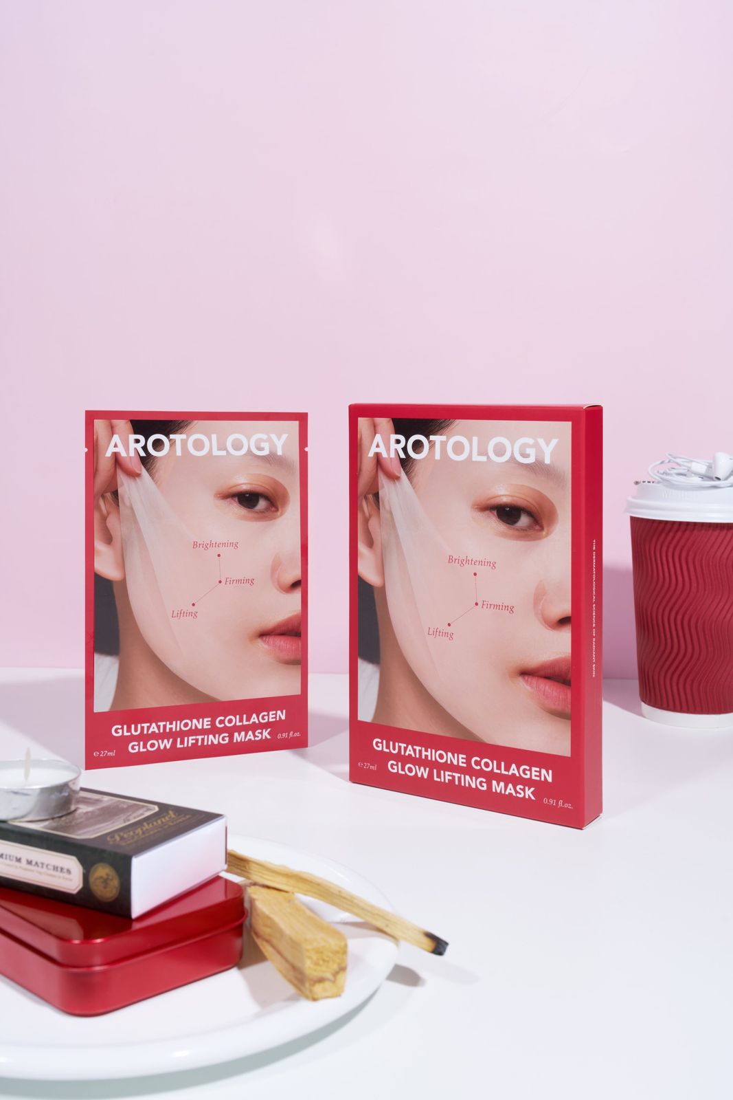AROTOLOGY · 마스크 — 캔들, 성냥, 틴케이스 등 라이프스타일 소품과 함께 패키지 2개를 배치한 연출컷, 핑크 배경