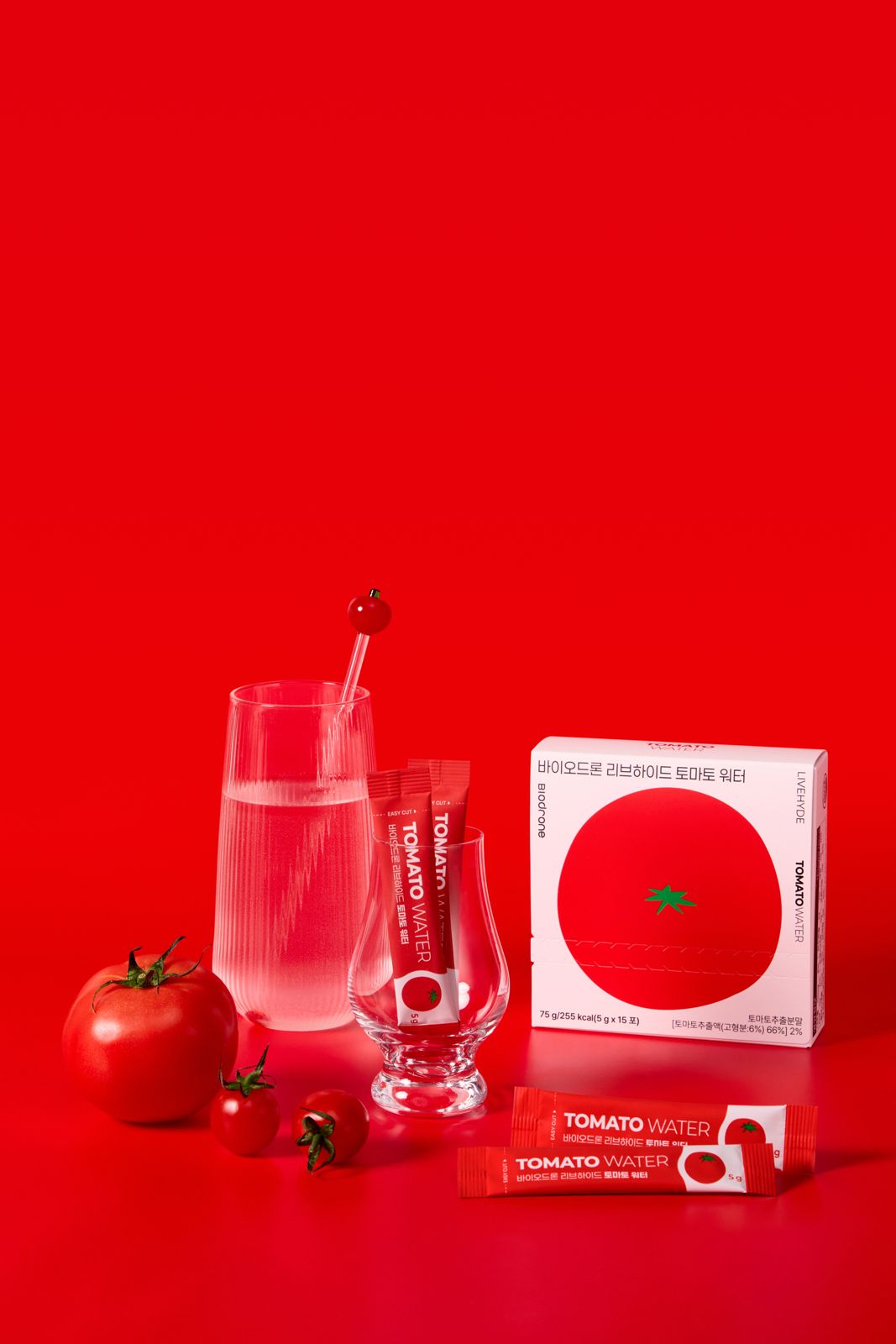 BIODRONE · 리브하이드 토마토워터 — 레드 배경에 유리잔·토마토·박스·스틱을 함께 연출한 컷