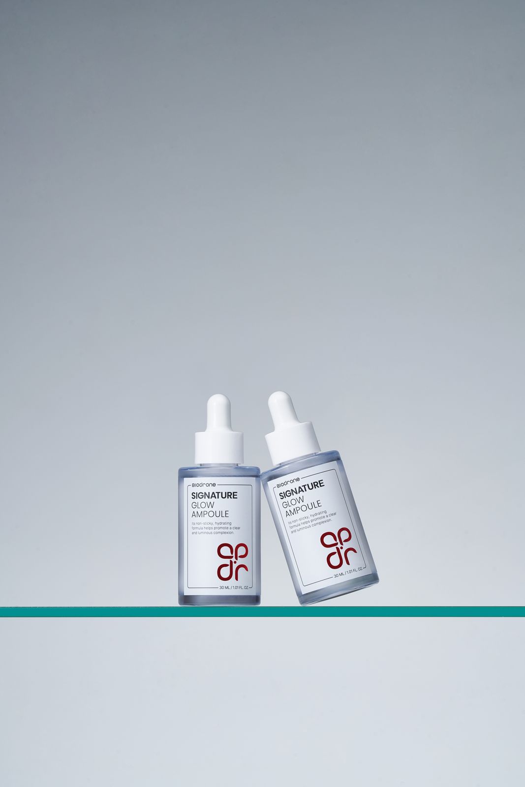 BIODRONE · 스킨케어 제품촬영 — 병 2개가 유리 선반 위에 서로 기댄 다이나믹 그룹컷