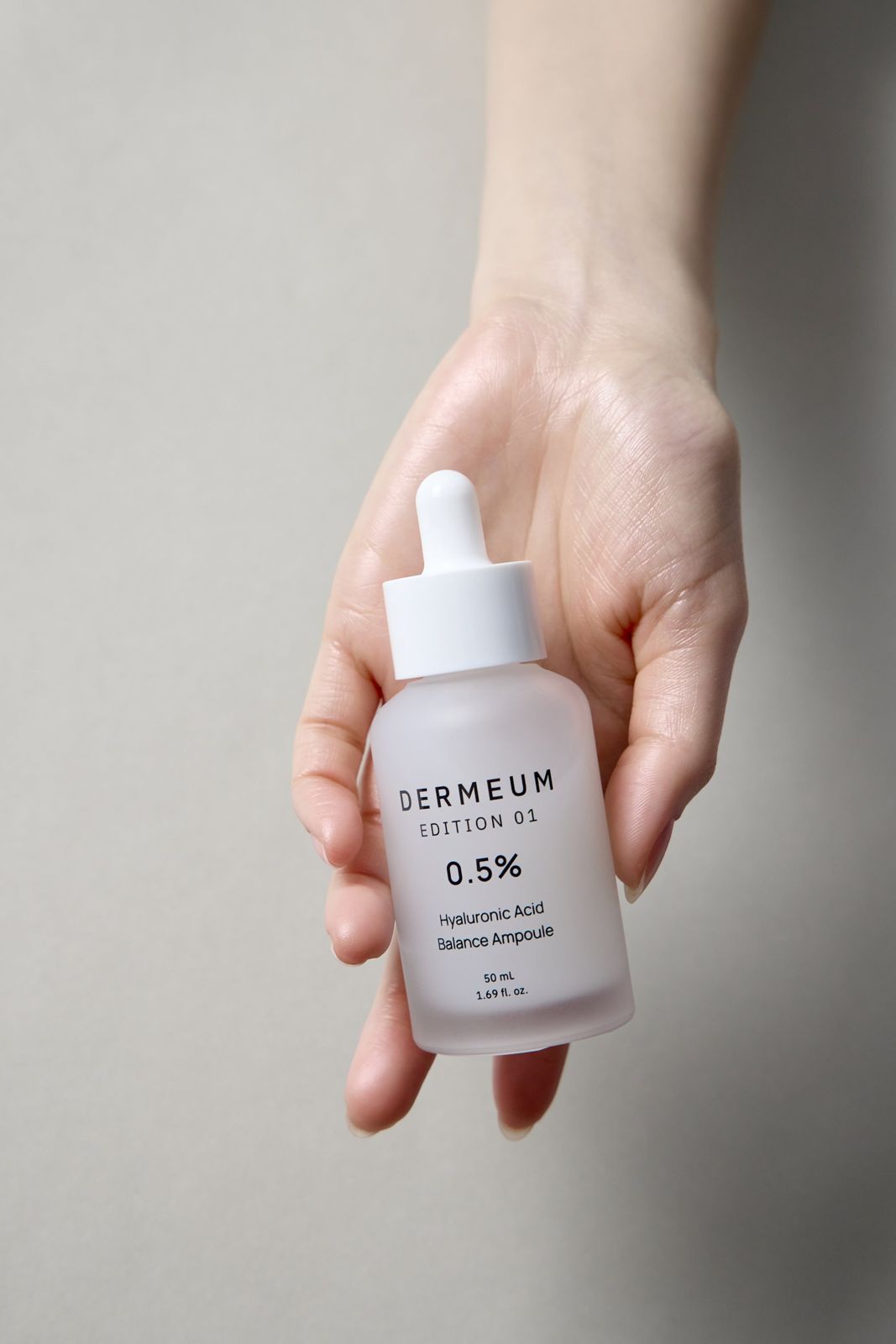 DERMEUM · 앰플 — 손바닥 위에 제품을 눕혀 들고 있는 핸드모델 컷, 그레이 배경