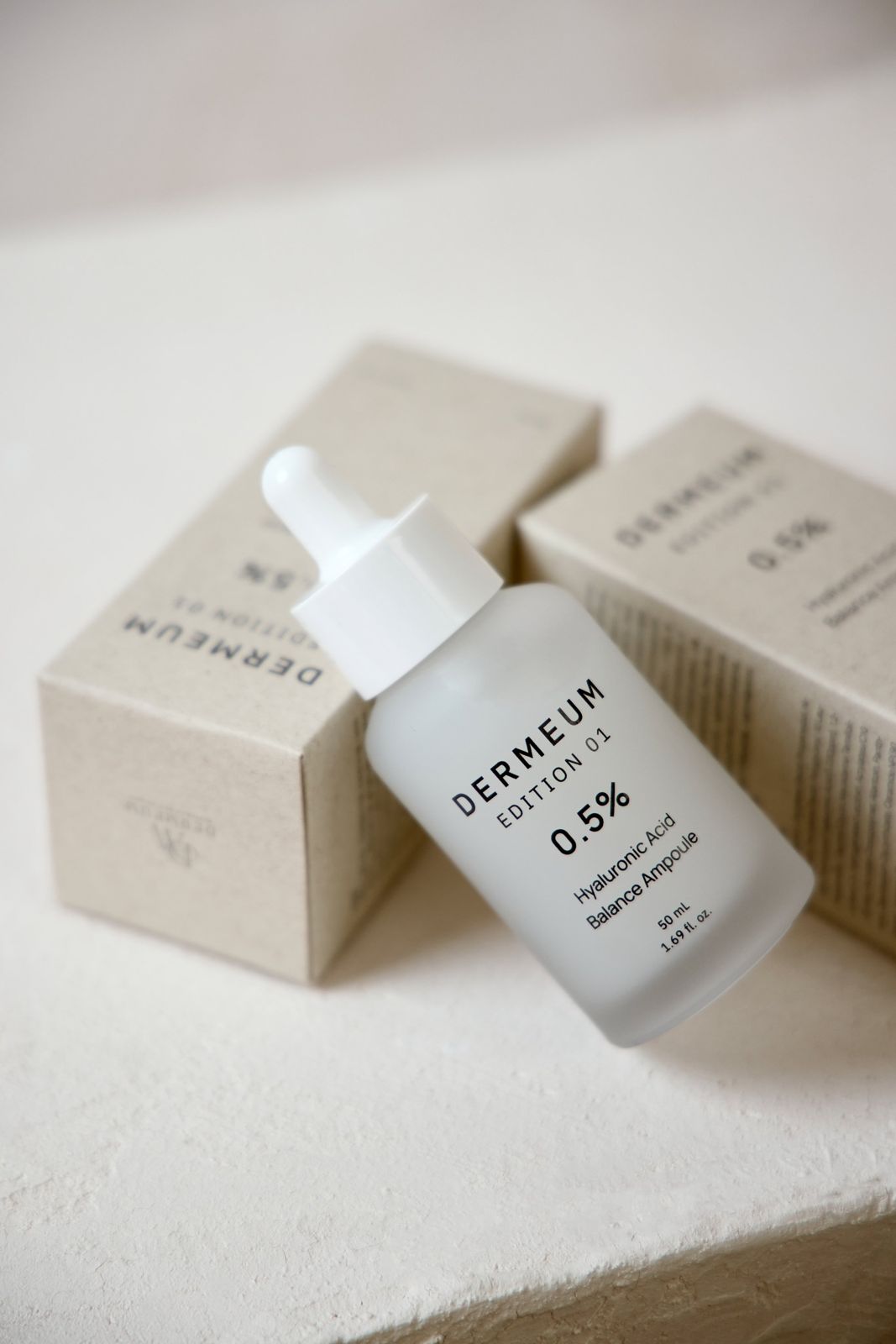 DERMEUM · 앰플 — 제품을 패키지 박스에 비스듬히 기대어 세우고 옆에 박스를 배치한 컷, 베이지 배경