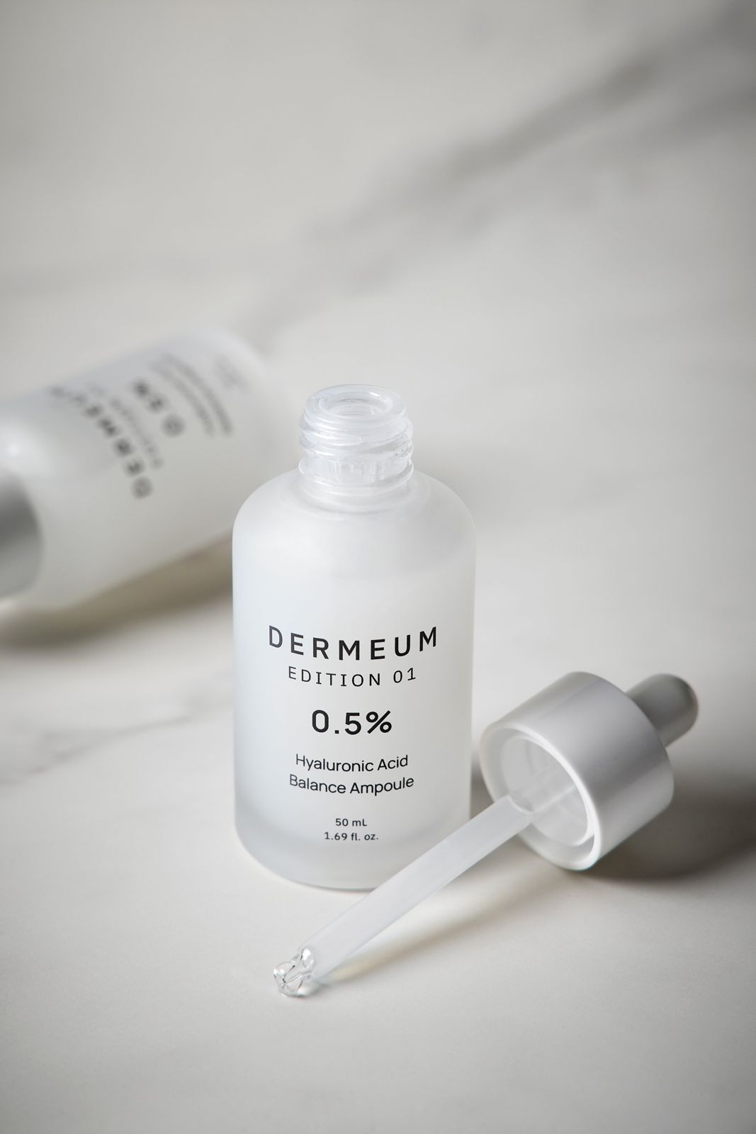 DERMEUM · 앰플 — 드로퍼를 뚜껑에서 분리해 눕혀두고 뒤로 다른 제품을 배치한 컷, 화이트 배경