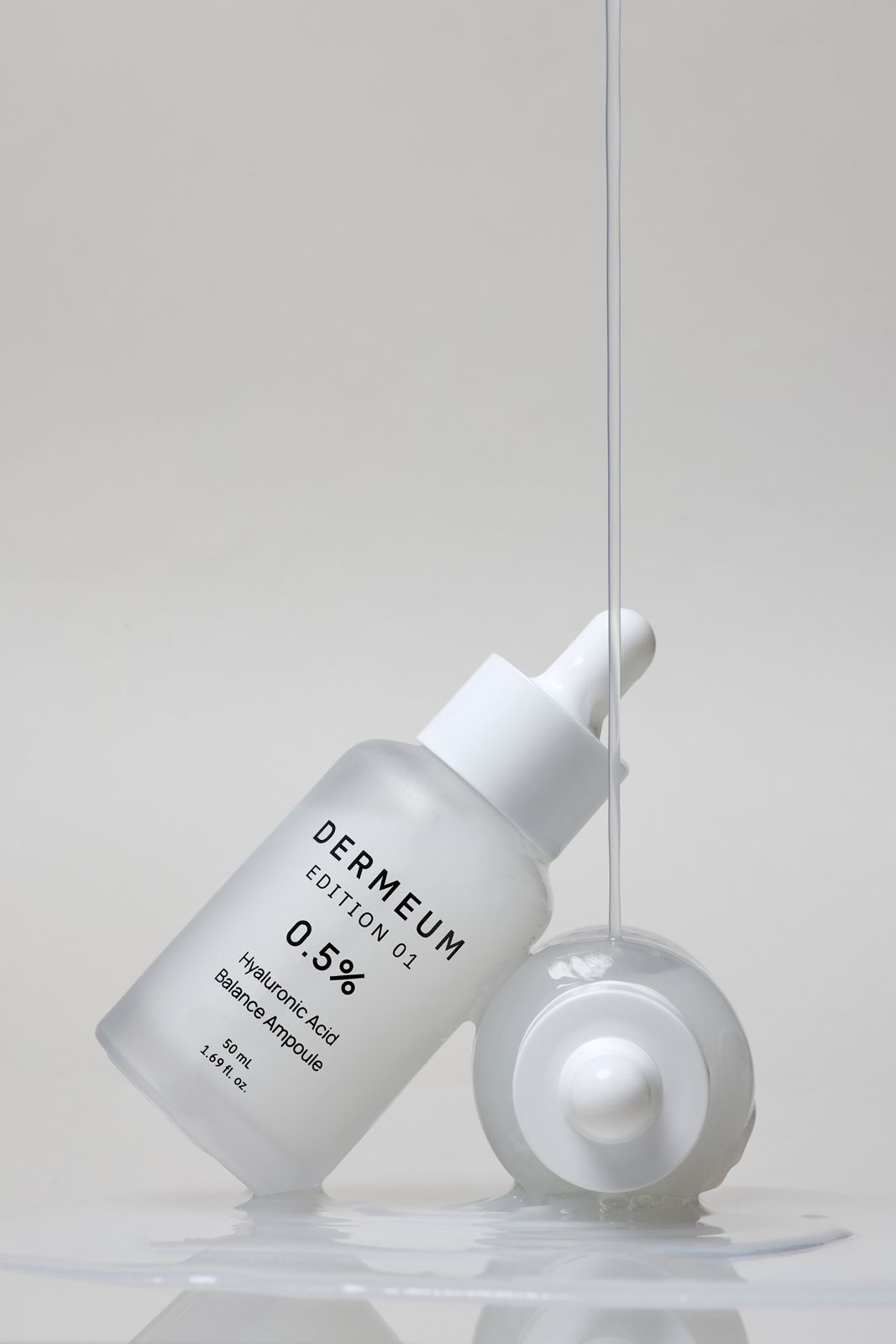 DERMEUM · 앰플 — 기울인 제품 위로 드로퍼에서 제형이 흘러내리는 텍스처컷, 다른 제품과 함께 배치, 화이트 배경