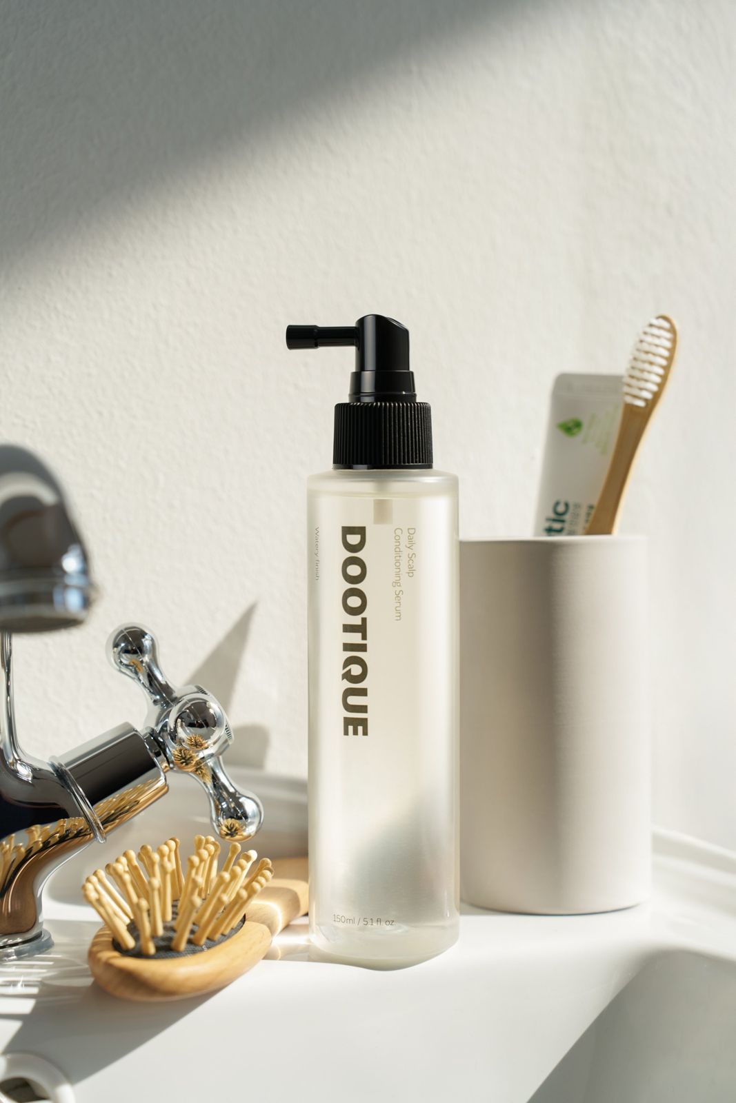 Dootique · 컨디셔닝세럼 — 욕실 세면대 위에 헤어브러시, 칫솔컵과 함께 놓인 라이프스타일 컷
