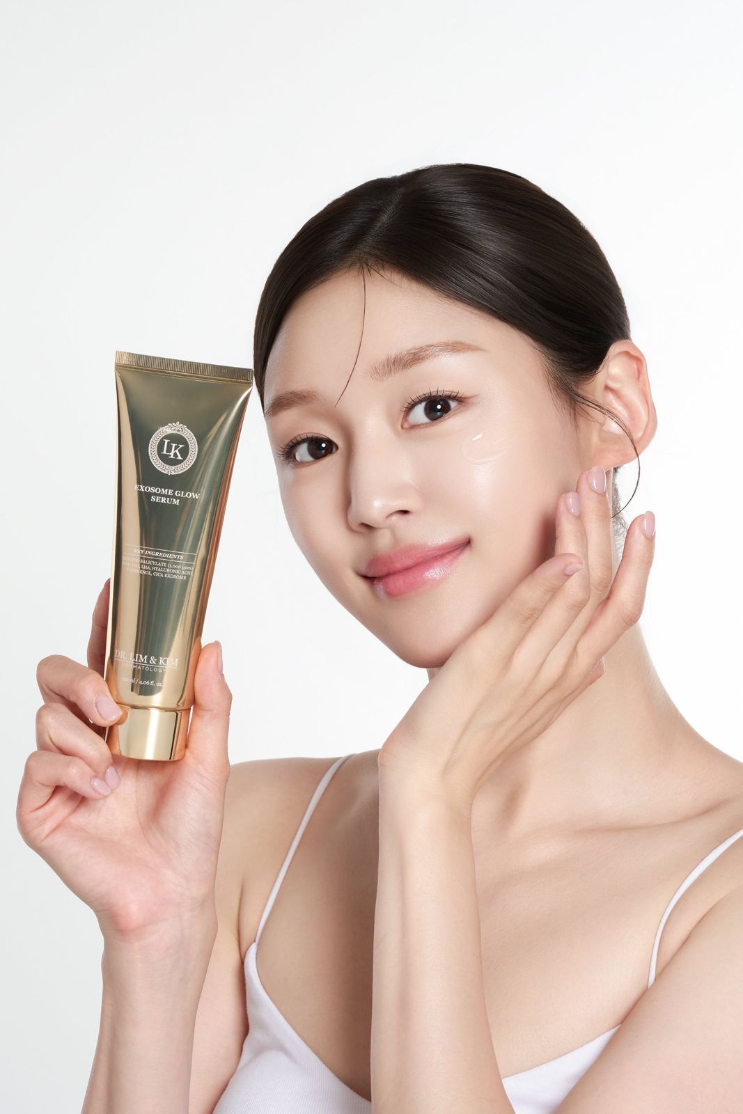 Dr Lim&Kim · 스킨케어 — 엑소좀 글로우 세럼 튜브를 들고 눈가에 세럼 제형을 바른 모습을 보여주는 텍스처 겸 모델 컷, 화이트 배경