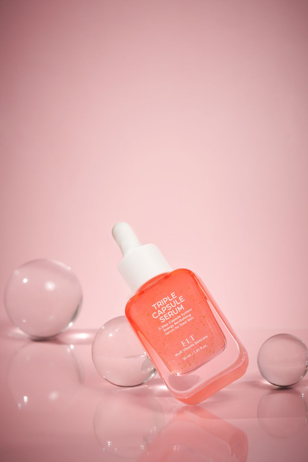ELT COSMETIC · 캡슐세럼 — 투명 유리구슬 소품들에 둘러싸인 기울어진 병 연출컷