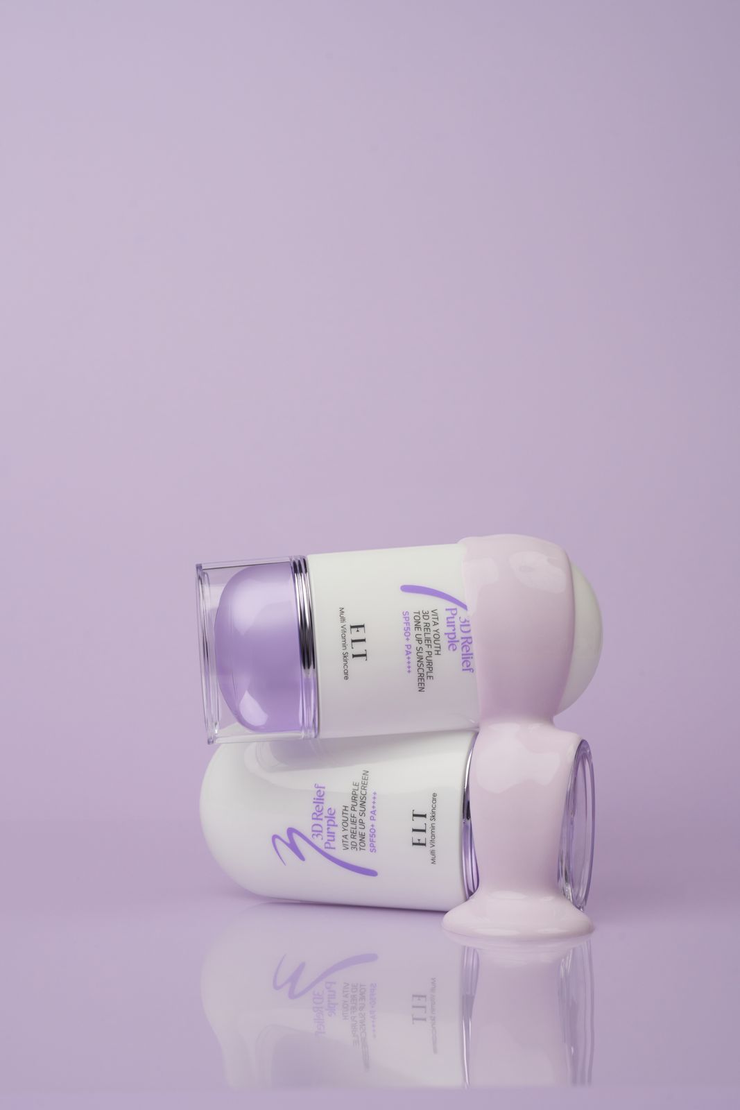 ELT COSMETIC · 선스크린 — 제품 2개를 십자로 겹쳐 쌓은 컷, 위쪽 제품 노즐에 텍스처가 맺힌 컷
