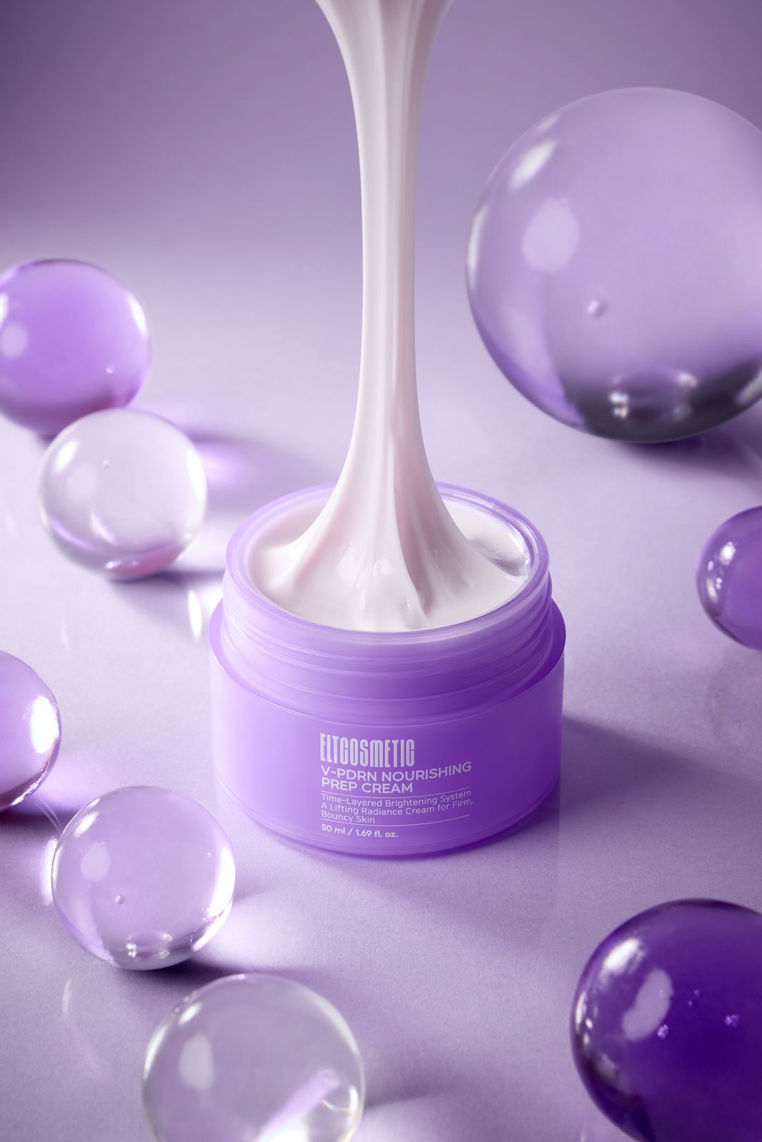 ELT COSMETIC · V-PDRN 크림 — 퍼플 배경에 다양한 크기의 투명·퍼플 수정토 구슬을 흩뿌리고 열린 용기에서 제형이 흘러내리는 연출컷