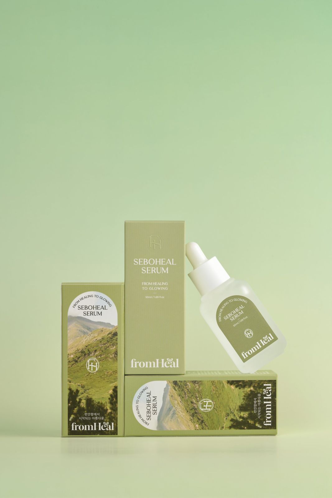 FROMHEAL · 세럼 — 패키지 박스 3개와 제품을 계단식으로 쌓아 배치한 기본 구성컷, 그린 그라데이션 배경