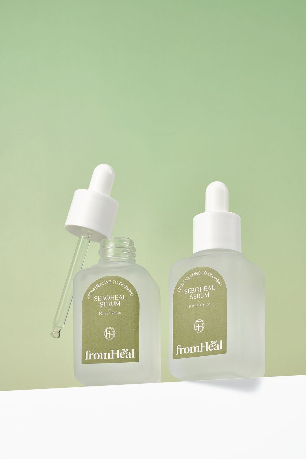 FROMHEAL · 세럼 — 드로퍼를 분리해 눕혀두고 제품 2개를 나란히 세운 컷, 그린 배경