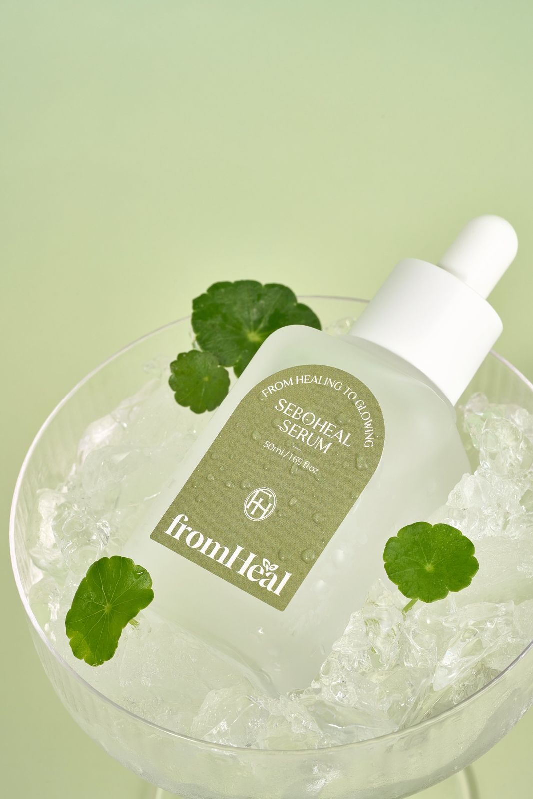 FROMHEAL · 세럼 — 얼음과 병풀잎을 채운 유리볼에 제품을 담은 연출컷, 그린 배경