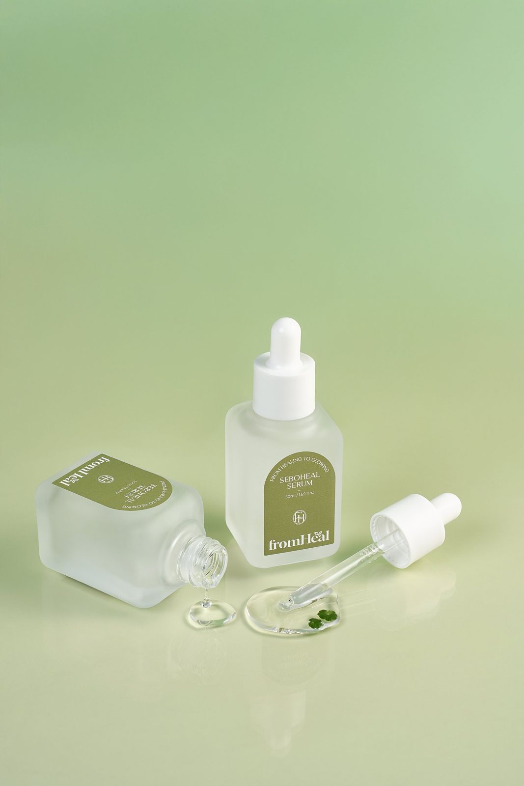 FROMHEAL · 세럼 — 뚜껑을 연 제품에서 제형이 흘러내리고 다른 제품과 나란히 놓은 텍스처컷, 그린 배경