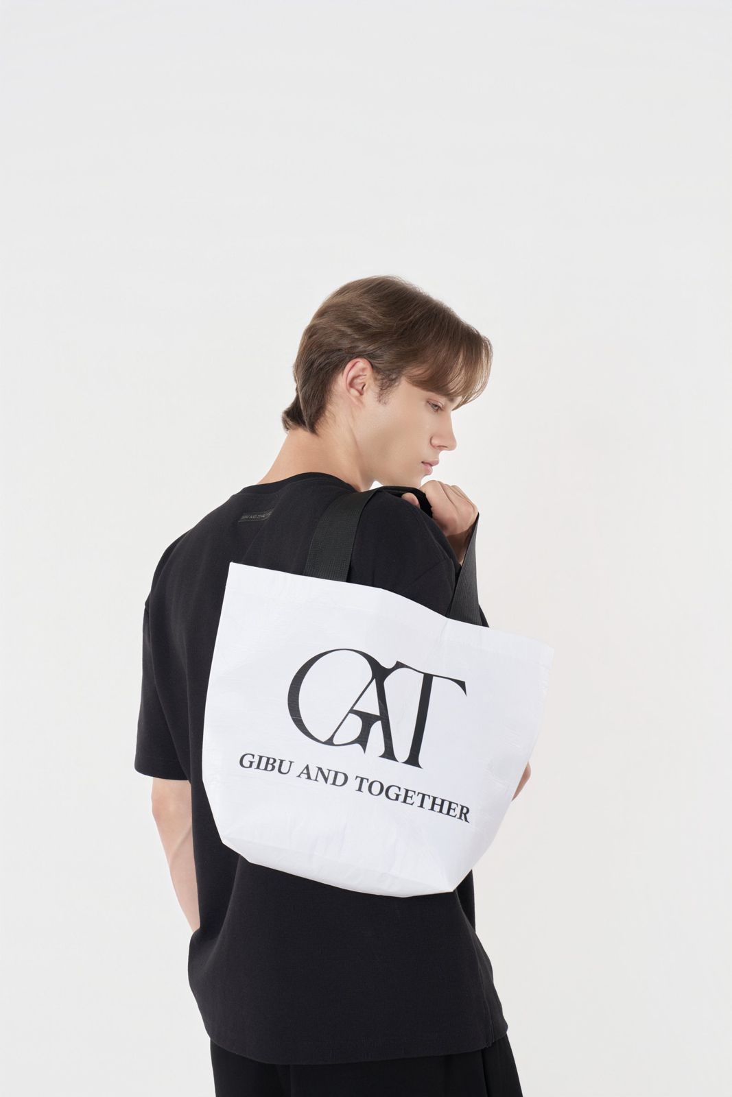 GAT · 티셔츠 & 팬츠 — GAT 로고 토트백을 어깨에 멘 모습을 보여주는 뒷모습 컷, 화이트 배경