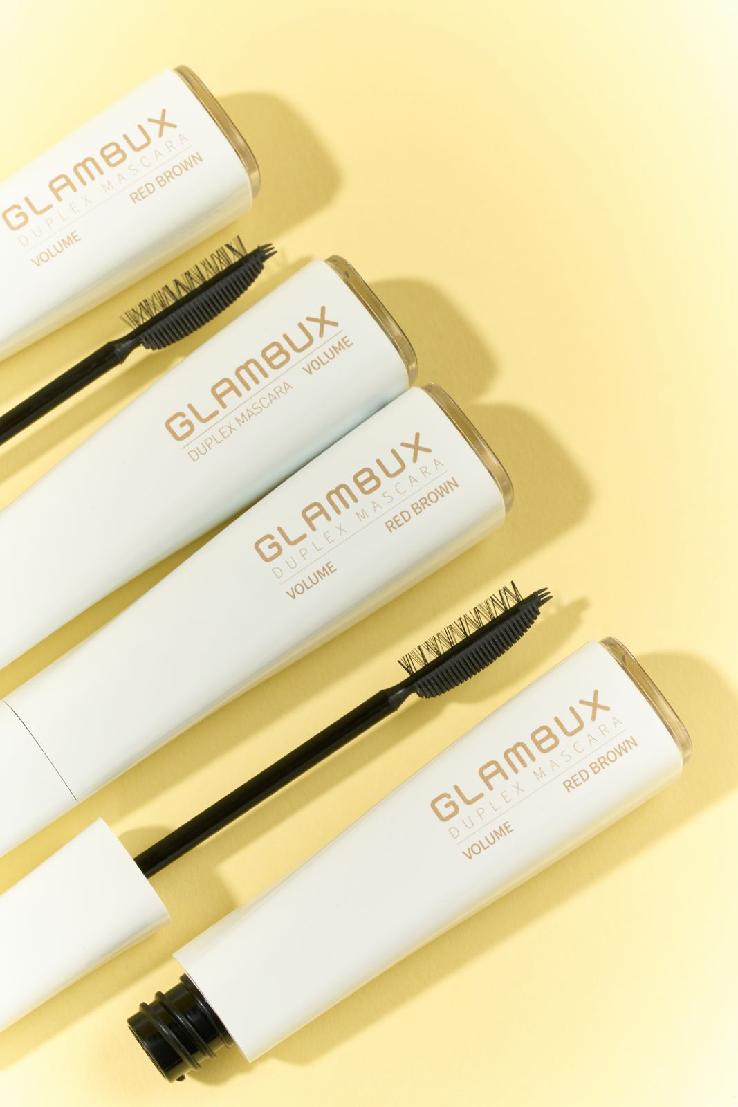 GLAMBUX · 마스카라 — 옐로우 배경, 레드브라운 톤 튜브 여러 개를 대각선으로 겹쳐 놓은 그룹컷