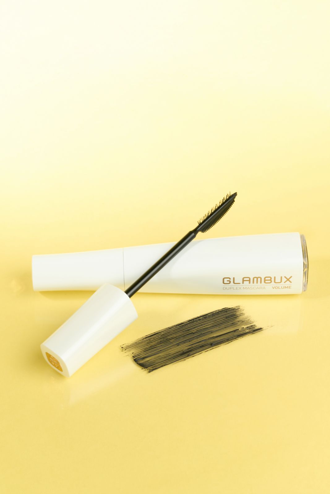GLAMBUX · 마스카라 — 옐로우 배경, 튜브와 브러시, 제형 스와치를 함께 배치한 컷