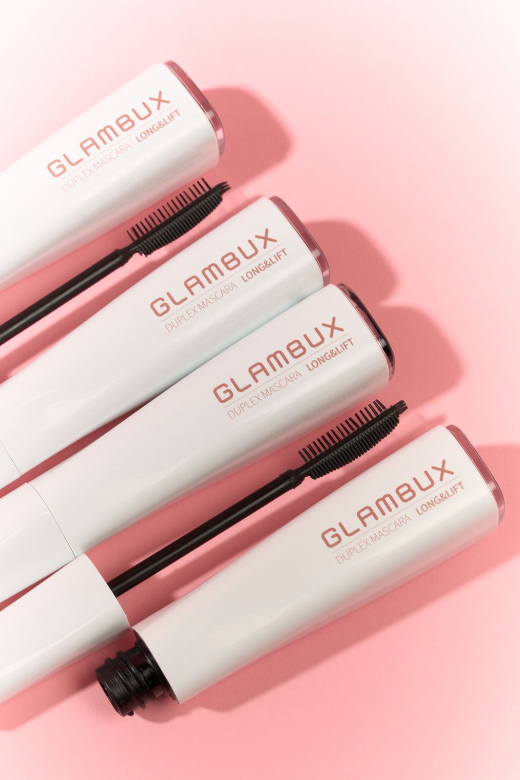 GLAMBUX · 마스카라 — 핑크 배경, 롱앤리프트 라인 튜브 4개를 대각선으로 겹쳐 놓은 그룹컷