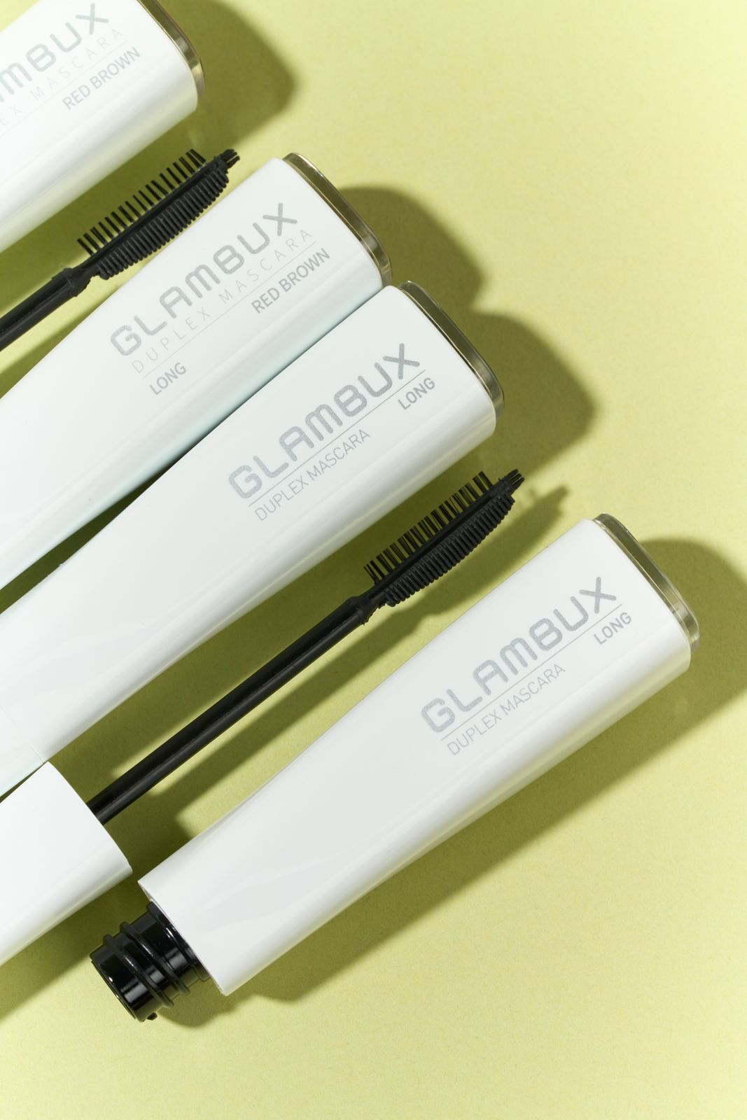 GLAMBUX · 마스카라 — 옐로우그린 배경, 롱/레드브라운 라인 튜브 여러 개를 대각선으로 겹쳐 놓은 그룹컷