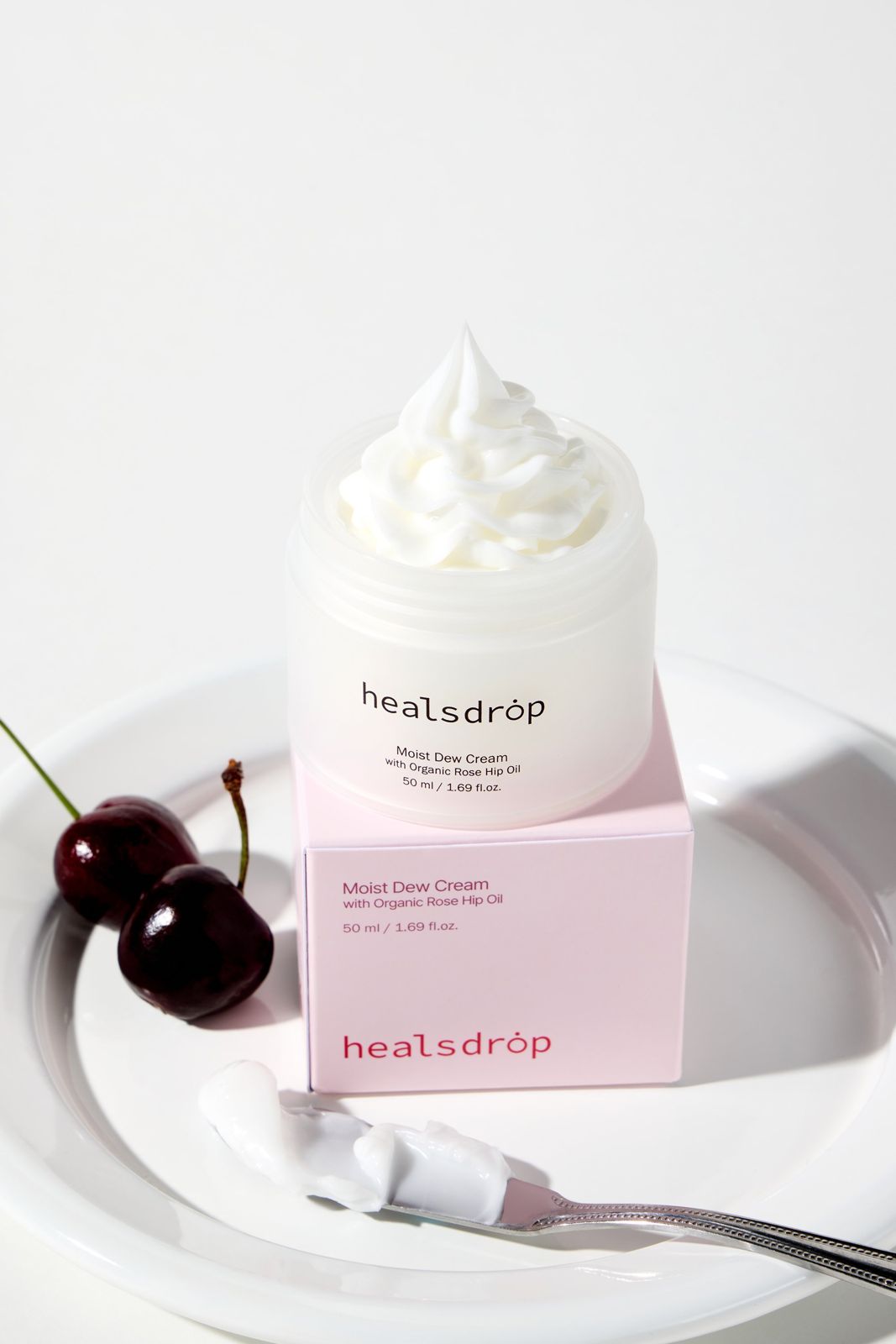HEALSDROP · 크림 — 뚜껑을 연 제품 위에 크림을 휘핑 모양으로 짜 올리고 체리를 곁들인 텍스처컷, 화이트 배경