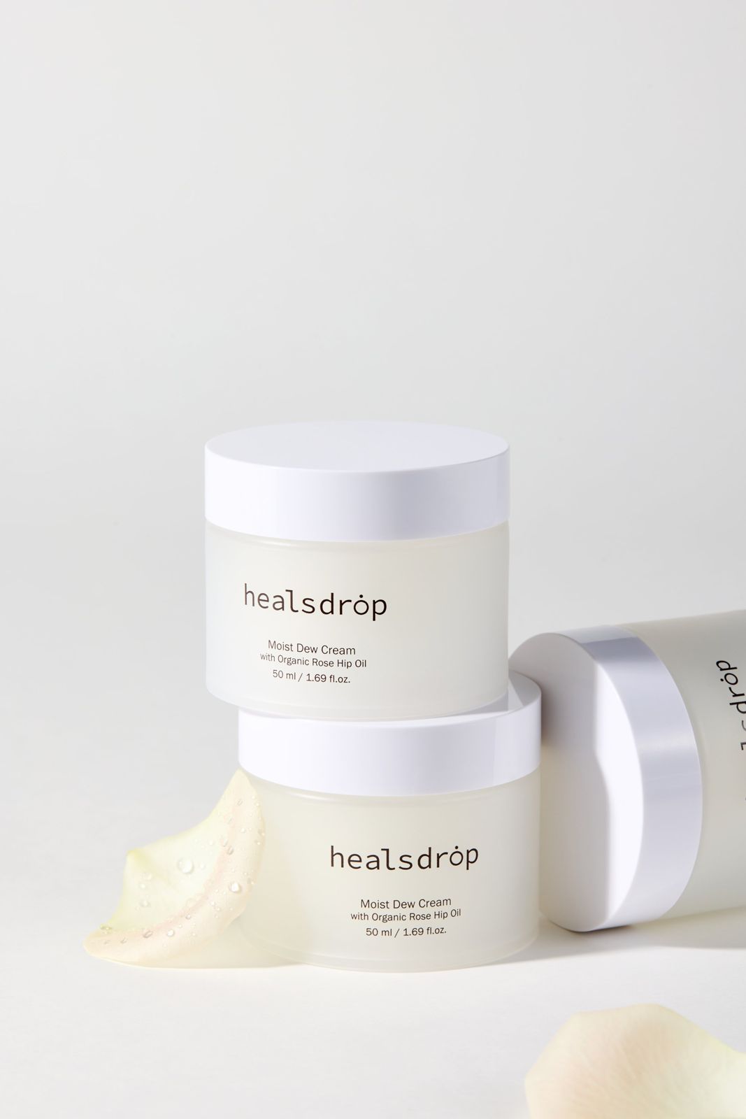 HEALSDROP · 크림 — 제품 2개를 쌓아 올리고 꽃잎을 곁들인 연출컷, 화이트 배경