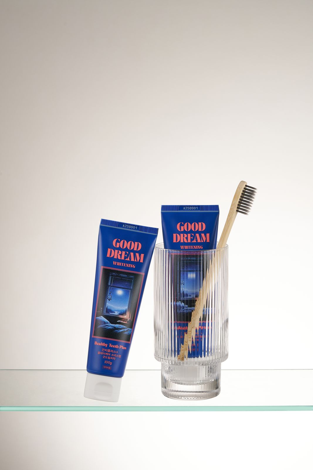 HEALTHY TEETH PLUS · 올데이케어 치약 — 굿드림 치약을 검정모 나무 칫솔·유리컵과 함께 놓고 다른 튜브는 선반에 눕힌 연출컷