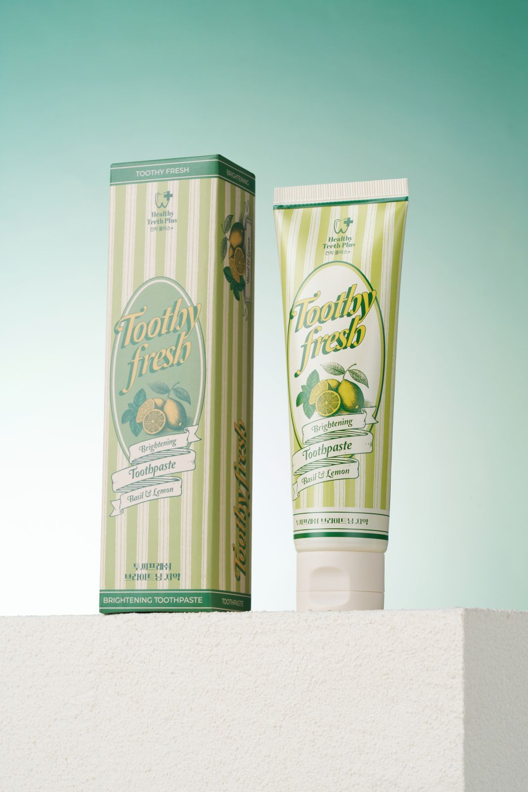 HEALTHY TEETH PLUS · 투씨프레시 브라이트닝 치약 — 민트 그라데이션 배경, 화이트 텍스처 좌대 위에 박스와 튜브를 나란히 세운 컷