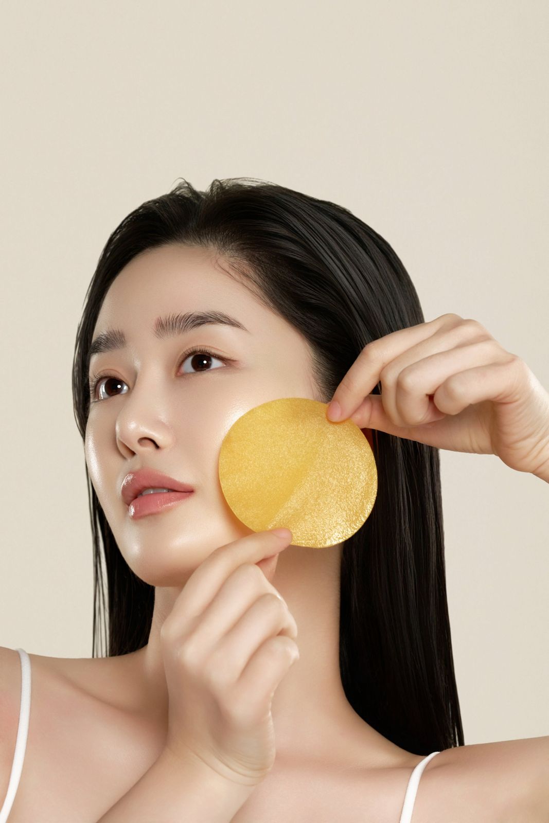 HEVEBLUE · 토너패드 — 패드를 뺨에 대고 있는 모델 뷰티컷, 베이지 배경