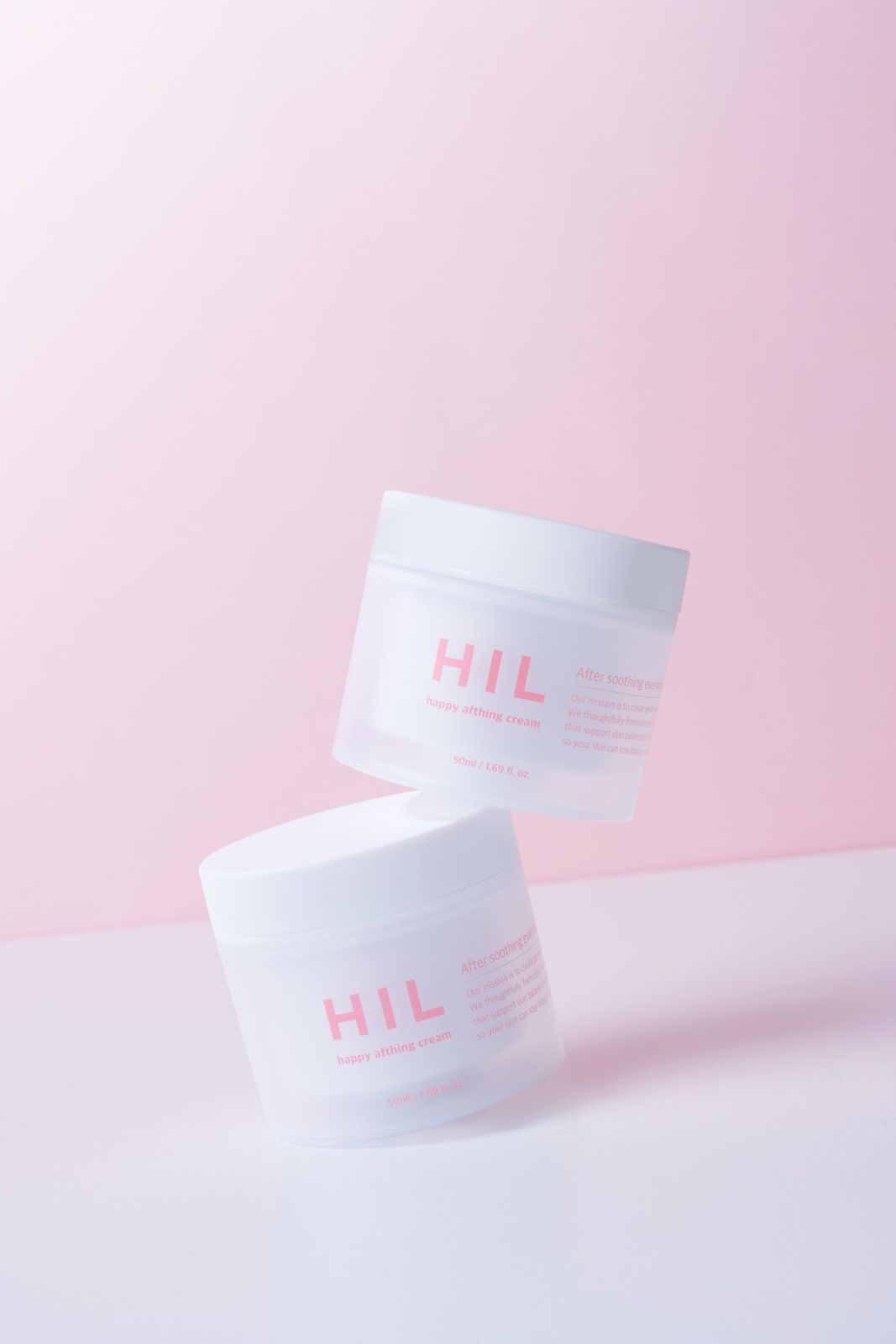 HIL · 크림 — 제품 2개를 비스듬히 쌓아 올린 연출컷, 핑크 그라데이션 배경