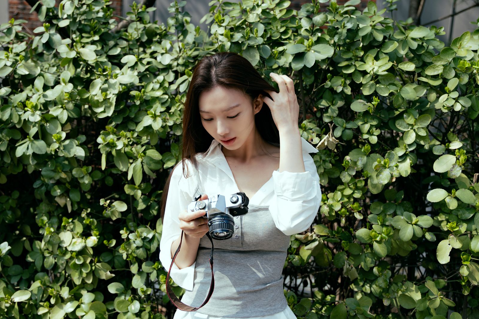 KINED · 모델촬영 — 초록 나무 배경 앞에서 빈티지 필름카메라를 들고 있는 컷