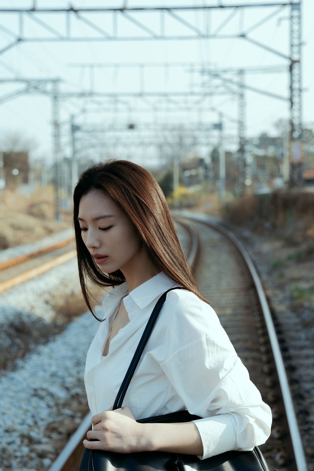 KINED · 모델촬영 — 철길 앞에서 가방을 멘 채 아래를 내려다보는 컷(제품 미노출)