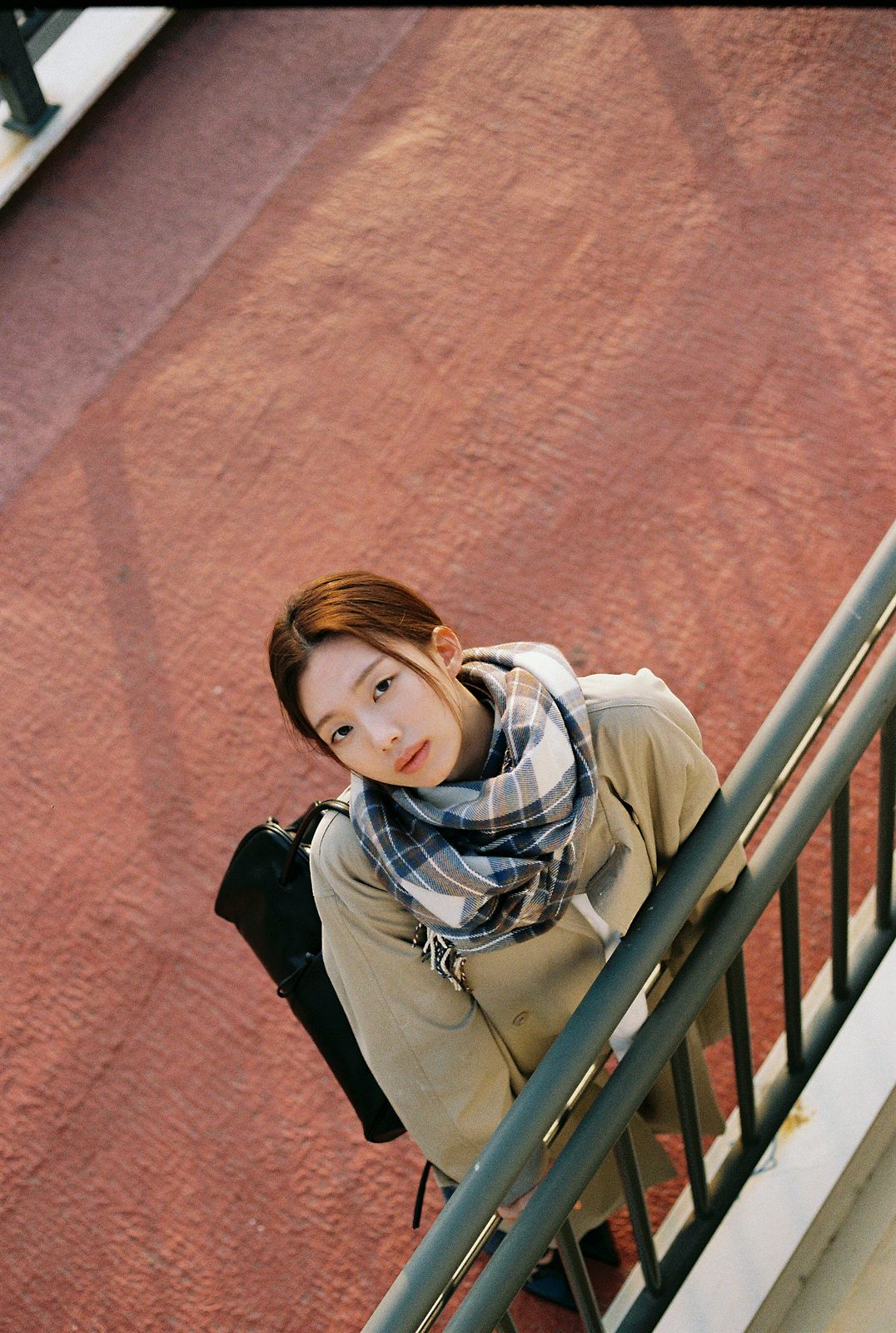 KINED · 모델촬영 — 붉은 벽 배경 계단에서 가방을 멘 채 위를 올려다보는 필름톤 컷(제품 미노출)