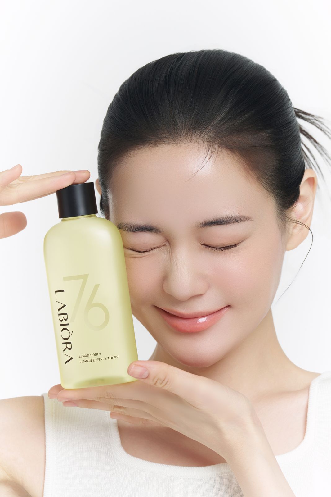 LABIORA · 레몬허니 스킨케어 (모델컷) — 동일 토너 병을 뺨에 대고 눈을 감은 채 미소 짓는 컷