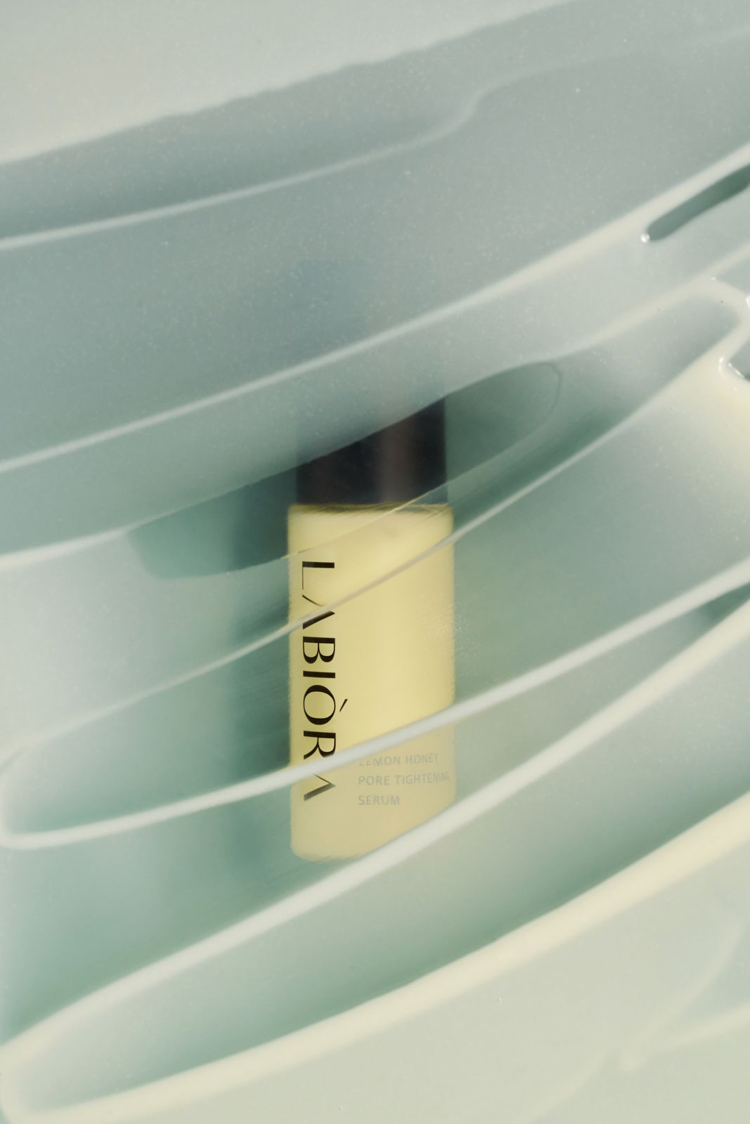 LABIORA · 레몬허니 스킨케어 — 민트톤 웨이브형 반투명 오브제 사이에 세럼이 놓인 연출컷