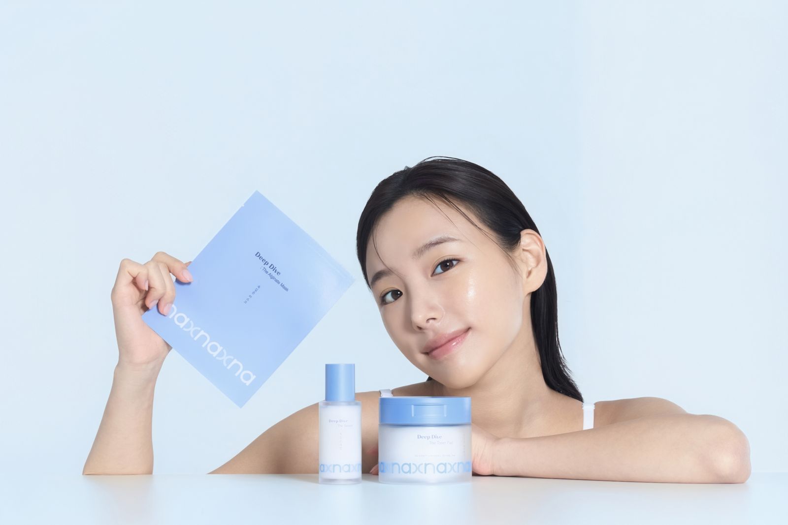 NAXNA · 모델촬영 — 마스크 파우치를 들고 테이블 위 토너·크림과 함께 라인업한 컷