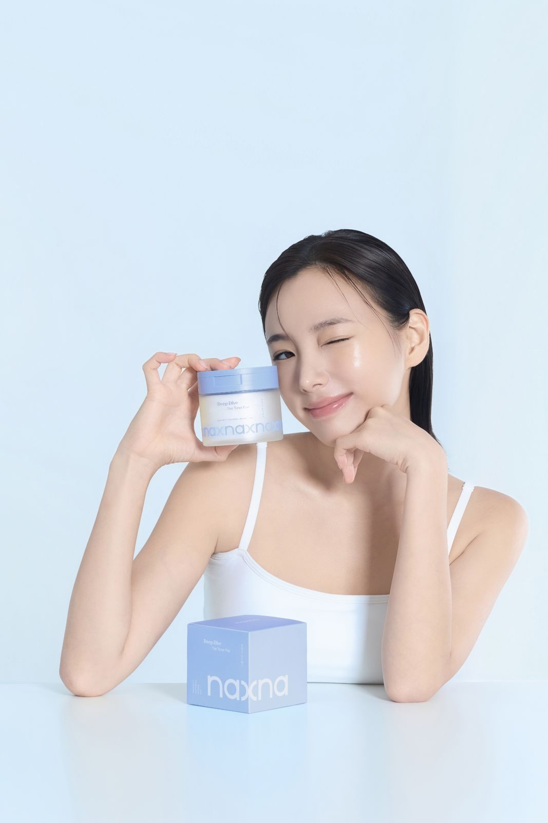 NAXNA · 모델촬영 — 크림 통을 들고 박스를 함께 둔 채 윙크하는 컷