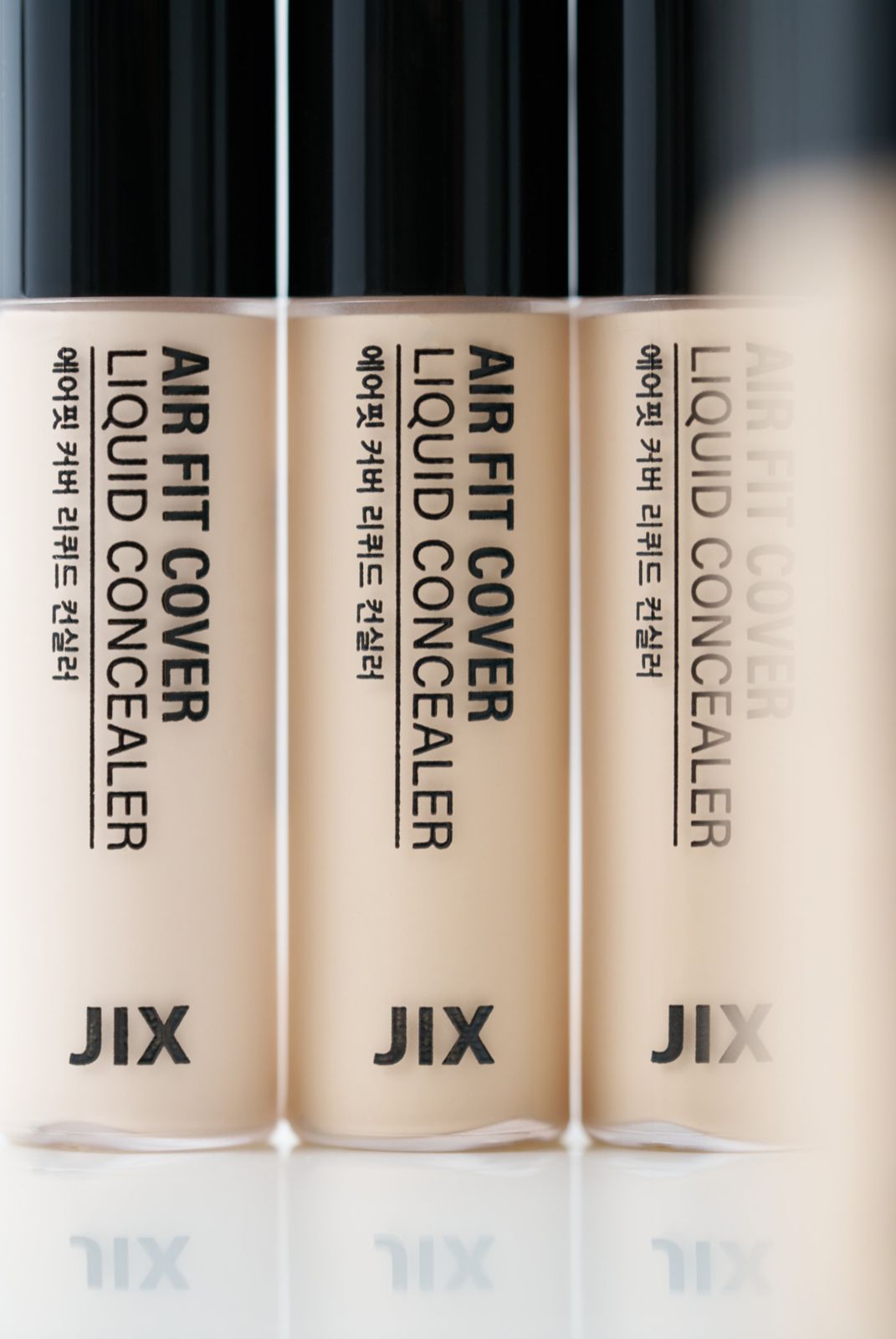 JIX · 컨실러 — 제품 3개를 나란히 세운 매크로 클로즈업, 블랙 배경, 하단 리플렉션