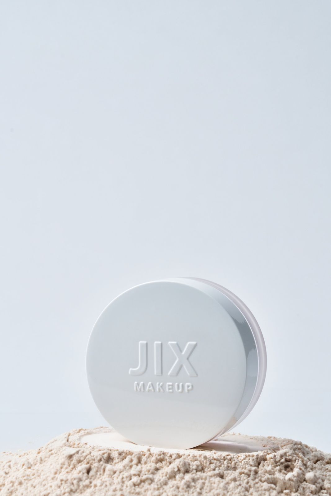 JIX · 파우더 — 제품을 파우더 더미 위에 세운 컷, 라이트블루 배경