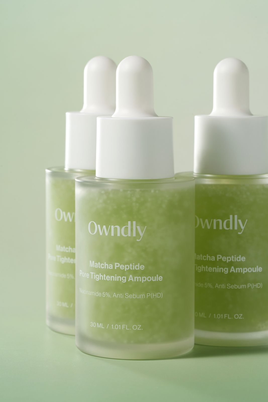 OWNDLY · 모공 타이트닝 앰플 — 병 여러 개를 대각선으로 배치한 그룹컷, 그린 배경