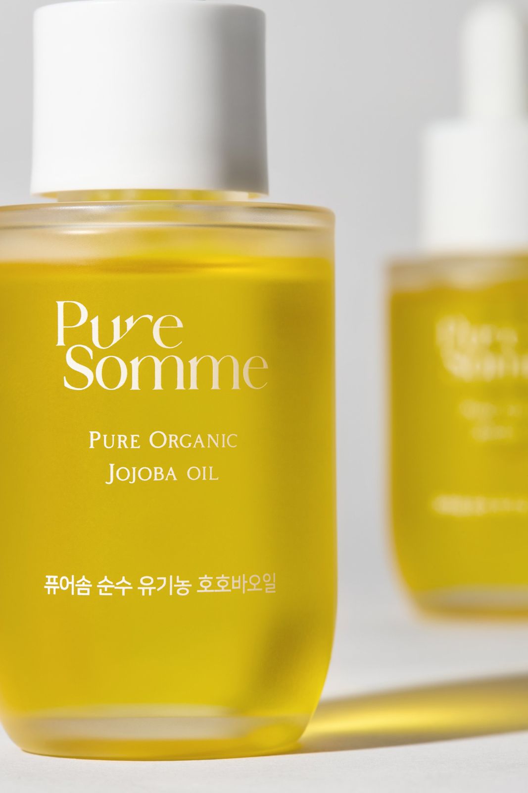 PURESOMME · 호호바오일 — 제품 2개를 클로즈업한 컷, 뒤쪽 제품은 블러 처리