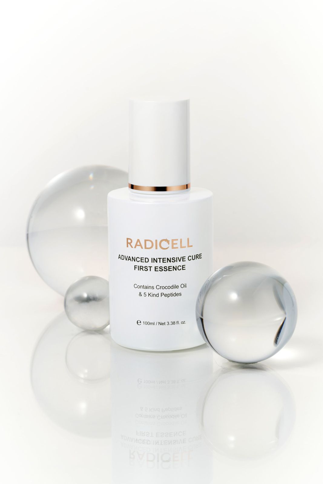 RADICELL · 인텐시브큐어에센스 — 투명 유리 구슬들 사이에 세운 연출컷, 리플렉션 바닥