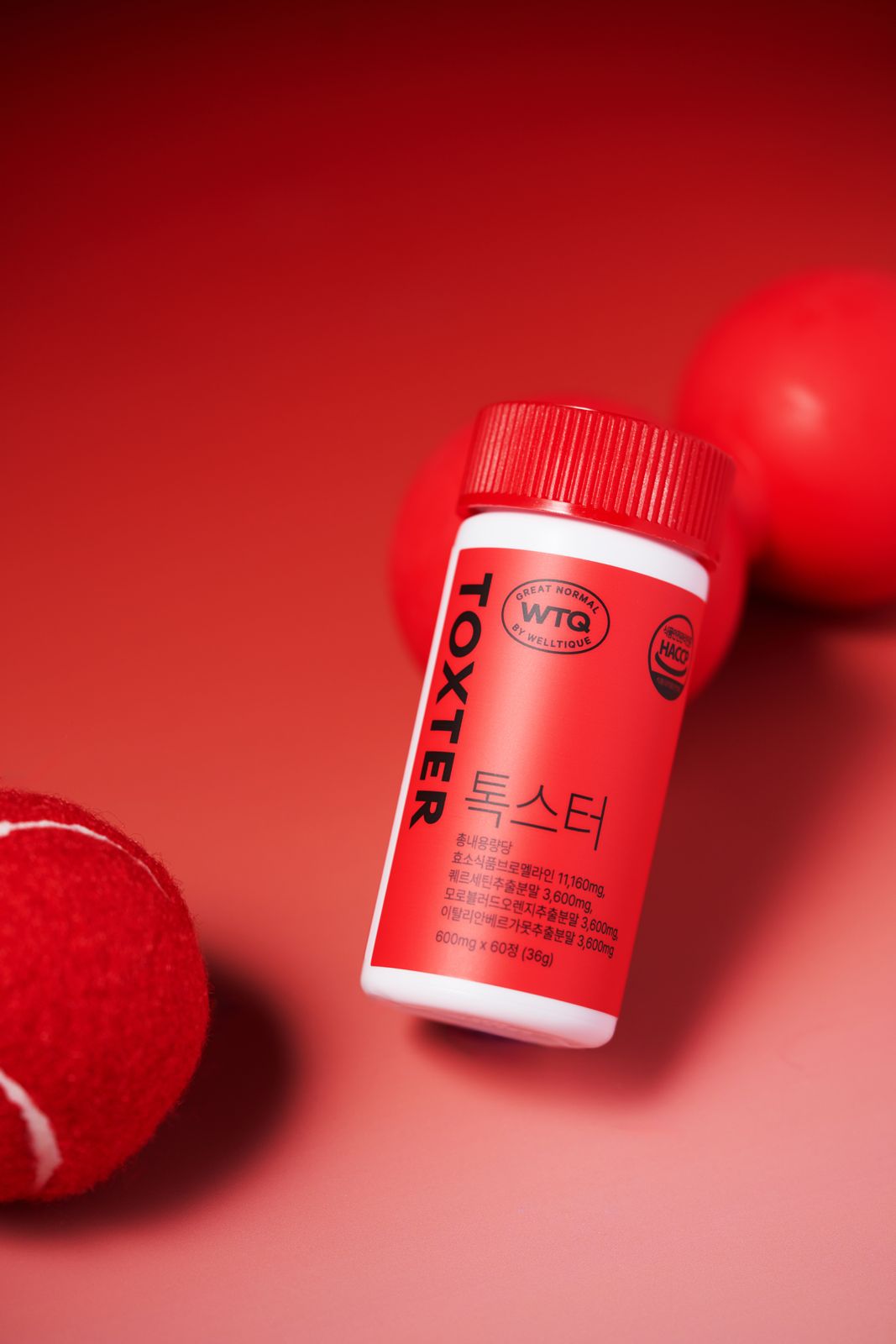 SH FOOD · 건강기능식품 — TOXTER 병을 비스듬히 눕히고 테니스공·덤벨을 배경에 배치한 로우앵글컷